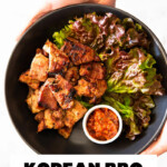 Holding a black bowl filled with Korean BBQ Pork, lettuce, and spicy dipping sauce with two hands.