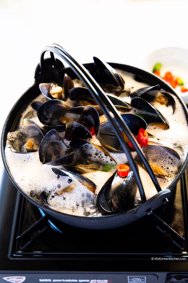 Mussel soup forming white bubbles in a black pot.