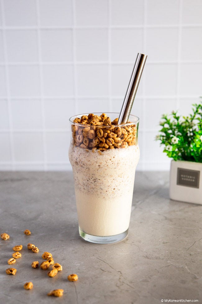 Front shot of Jolly Pong Shake in a large glass, a few Jolly Pongs scattered nearby. A small plant in the background.