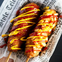 Two Korean corn dogs lay next to each other on waxed paper.