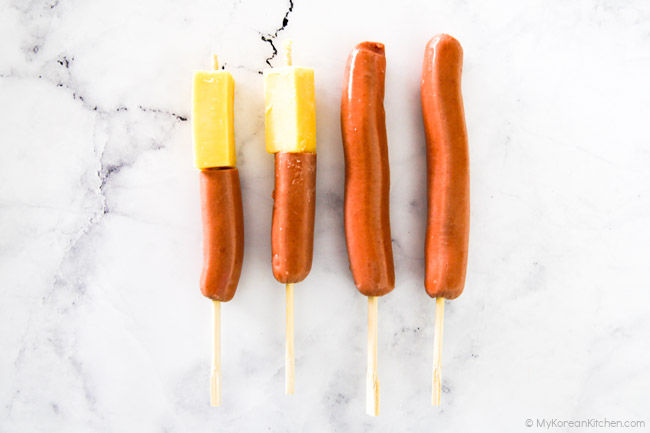 Four sausages are skewered on wooden chopsticks.