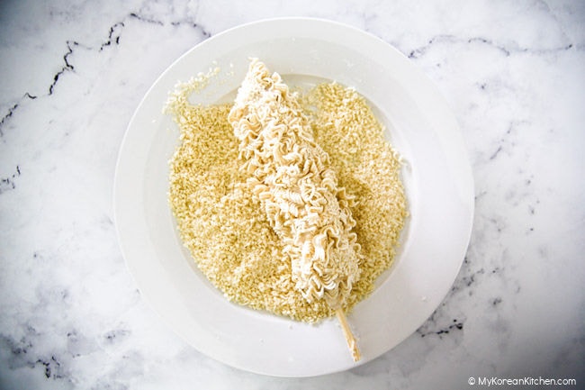 Breading a battered corn dog with panko breadcrumbs.