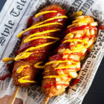 Two Korean corn dogs lay next to each other on waxed paper.