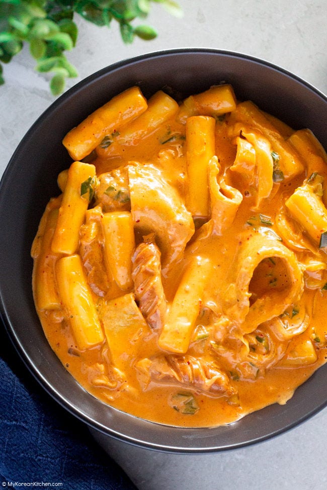 A close-up photo of rose tteokbokki served in a black pasta bowl.