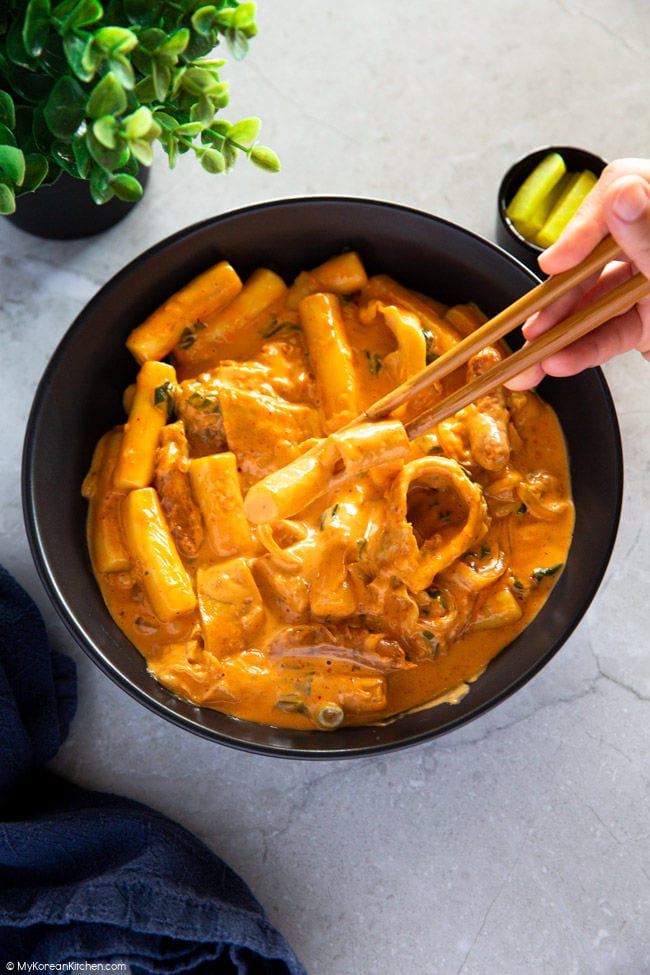 Holding a rose sauce-coated fish cake and tteokbokki with chopsticks.