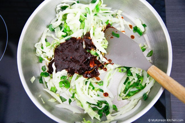 Adding tteokbokki sauce to the stir-fried vegetables in a pan.
