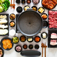 A vertical photo of a Korean BBQ table set up with various side dishes and meat.