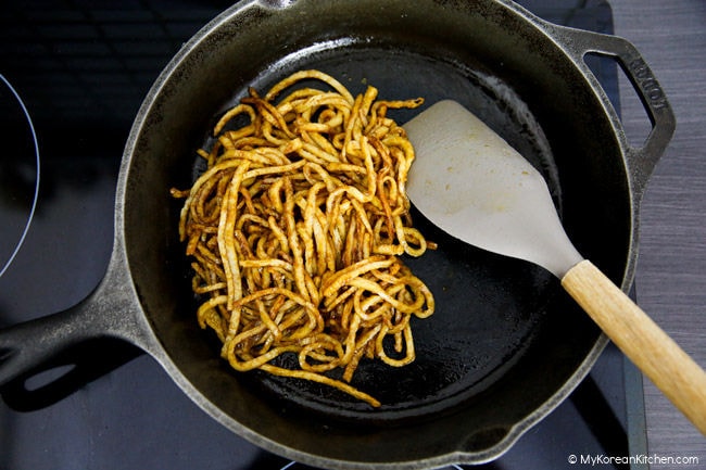 Stir frying fish cakes in a skillet with sauce.
