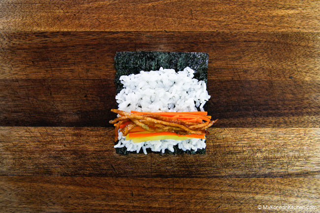The ingredients for mini kimbap are assembled and placed on a wooden board, ready to be rolled up.