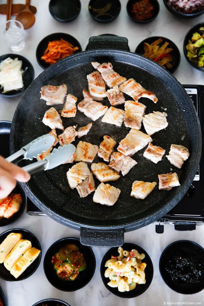 Turning the pork belly BBQ with tongs over the grill pan.