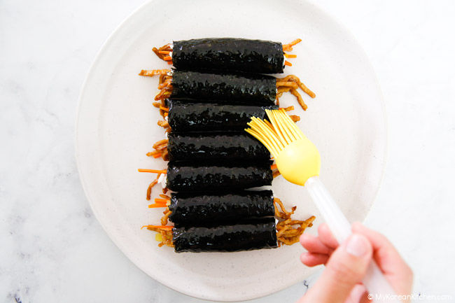 Lightly brushing sesame oil over each mini kimbap using a yellow silicone brush.