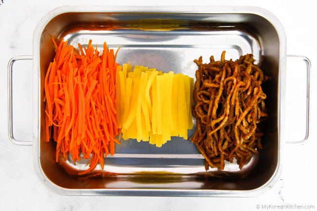 Three different kimbap fillings - lightly stir fried carrots, yellow pickled radish, stir fried fish cakes, prepared in a stainless steel tray.