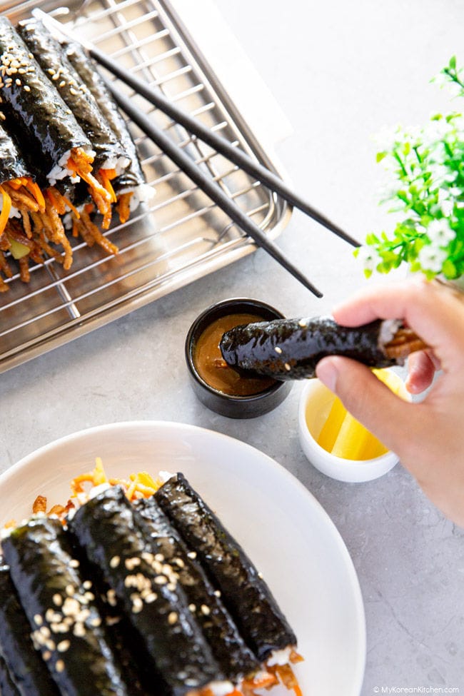 Dipping a mini kimbap into the bowl of mini kimbap dipping sauce.