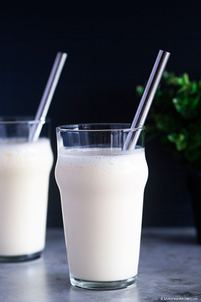 Close-up image of two glasses containing blended makgeolli shakes, accompanied by stainless steel straws.