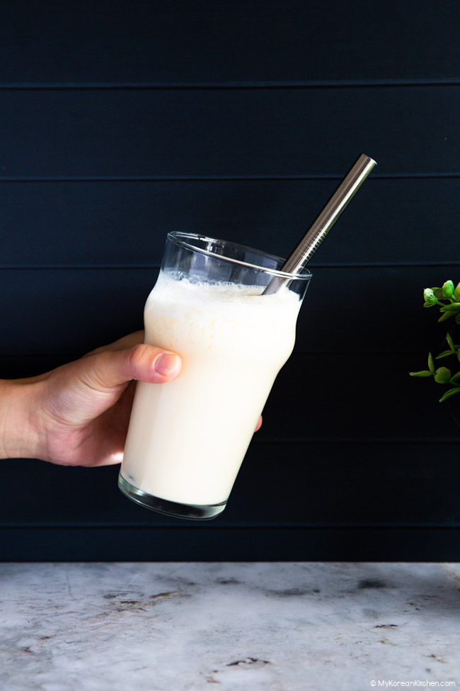 Holding a glass of blended makgeolli shake in one hand.