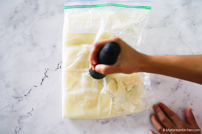 Gently crushing shaved ice using a pestle in a zip-lock bag.