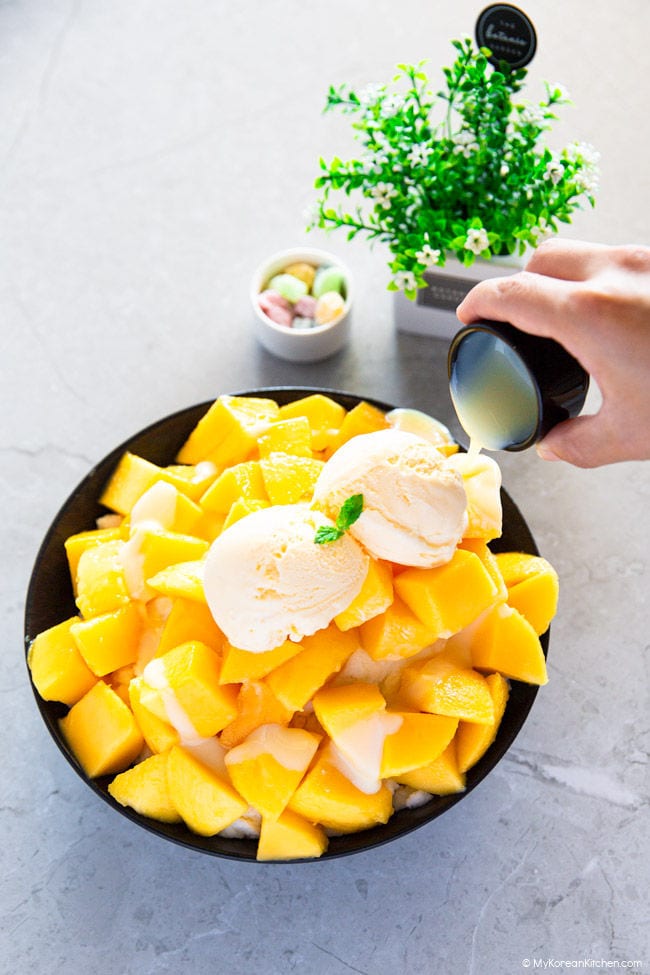 Glazing sweetened condensed milk over a pile of sliced mangoes in a black bowl