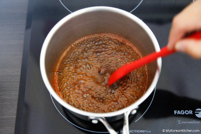 Boiling the sotteok sotteok sauce ingredients in a small saucepan and stirring with a red silicone spatula.