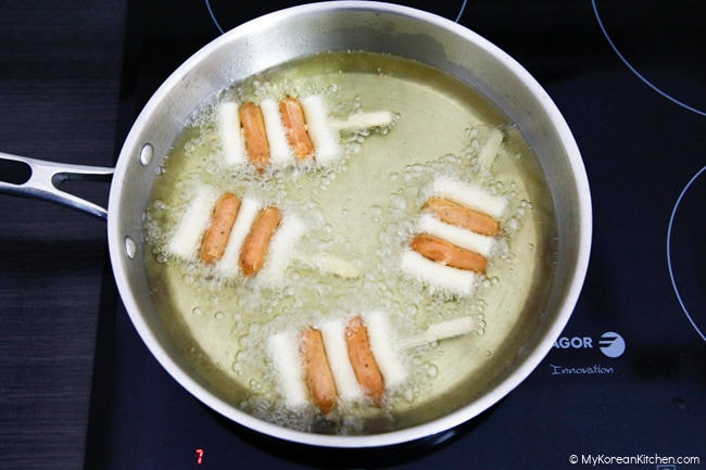 Deep frying the sotteok sotteok skewers in a stainless steel skillet.