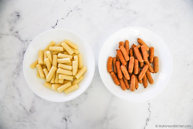 Two white bowls filled with Korean rice cakes and mini sausages