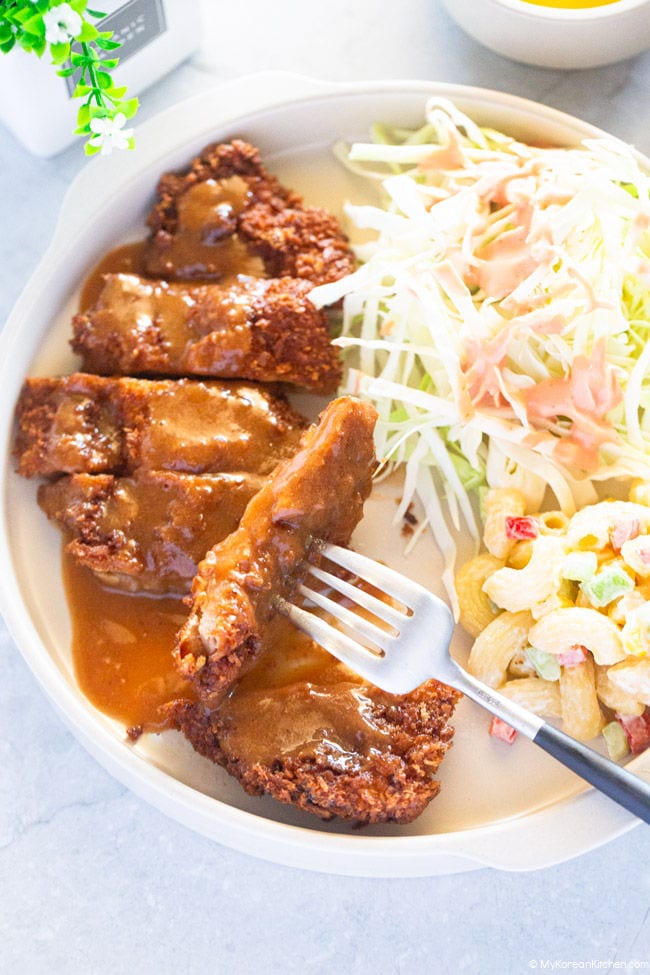 Sliced donkatsu positioned on the left side of the plate. On the other side of the plate, there's shredded cabbage and macaroni salad.