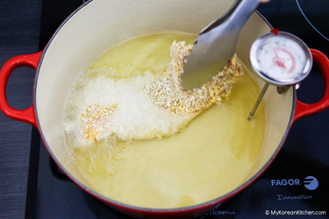 Using stainless steel tongs to place a panko-breaded pork cutlet into a pot filled with hot oil.