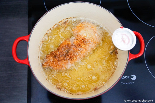 Pork cutlet being deep-fried in a pot of hot oil to golden brown.