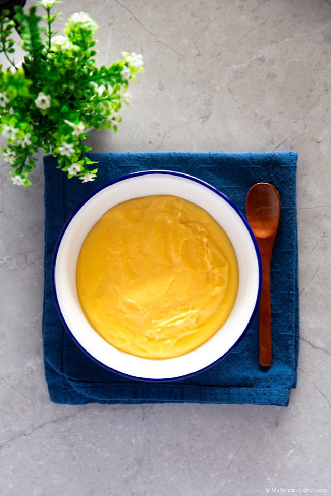 A bowl of vanilla custard placed on a blue napkin, with a wooden spoon resting on the side.