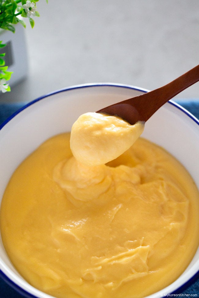 A hand holding a wooden spoon, scooping vanilla custard from a serving bowl.