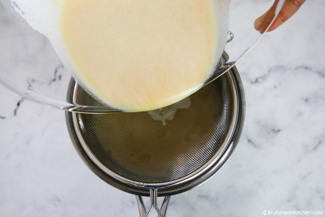 Straining the custard mixture into a stainless steel bowl.