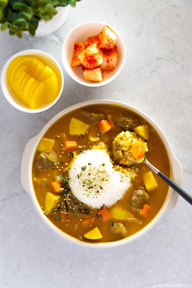 A spoonful of Korean curry rice is placed on a plate of curry.