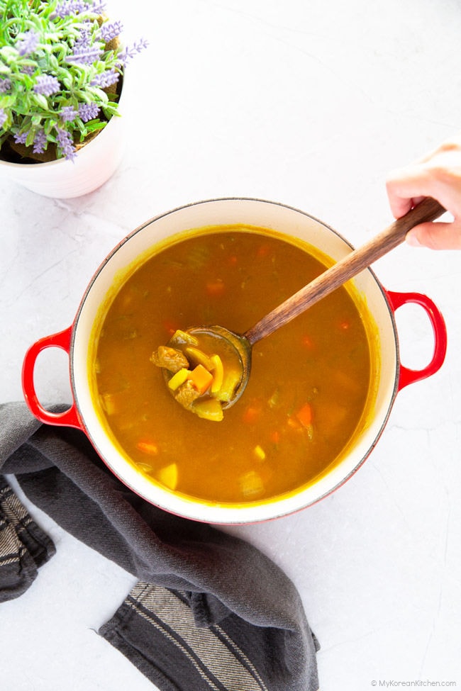 Scooping curry with a wooden spoon from a large pot of curry
