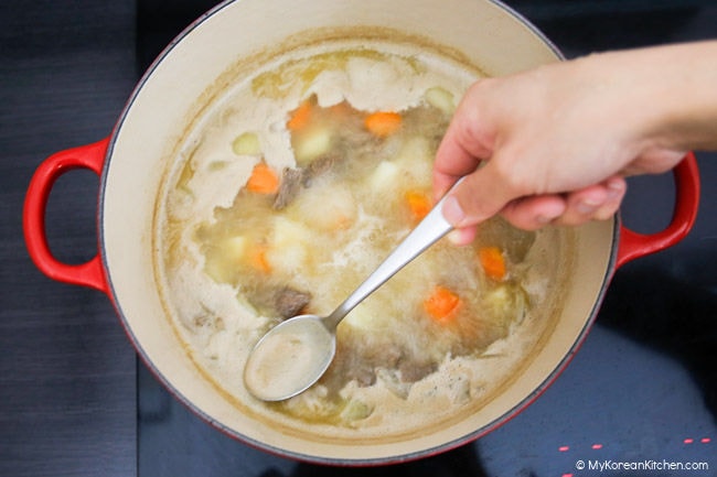 Scooping scum with a spoon from a boiling pot.