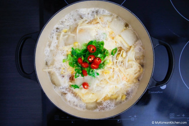 Dried pollack and radish boiling in a Dutch oven pot, garnished with beaten egg, chopped green onions, and red chilies.