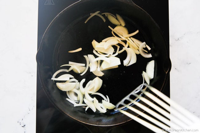 Stir-frying sliced onions in a skillet.