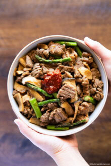 Holding a bowl of cooked Korean BBQ pork with vegetables in two hands.