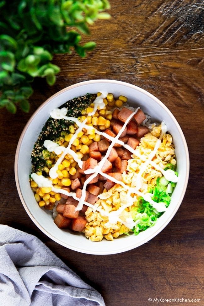 A bowl of Spam Egg Mayo Rice Bowl topped with neatly arranged green onions, egg, Spam, corn, and drizzled with mayo.