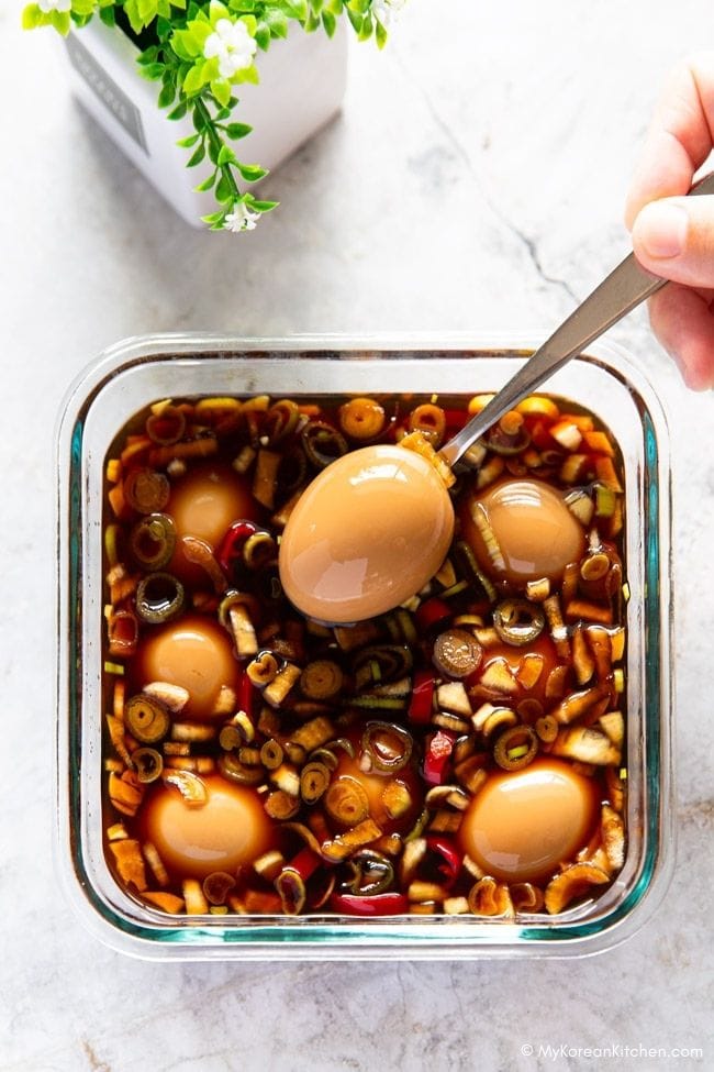 Lifting a 24-hour marinated egg with a spoon from the square container.