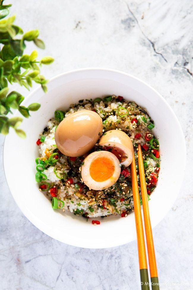 Marinated eggs over a bed of rice, one egg halved and another whole, with chopsticks resting on the bowl.