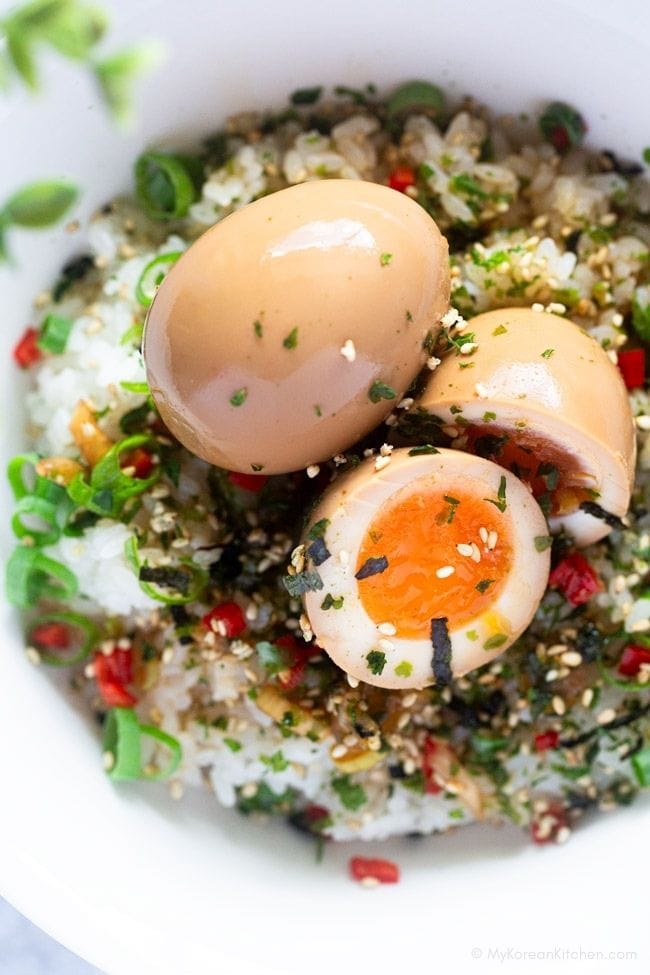 Two eggs on a bed of rice, including one halved, topped with seaweed and sesame seeds.