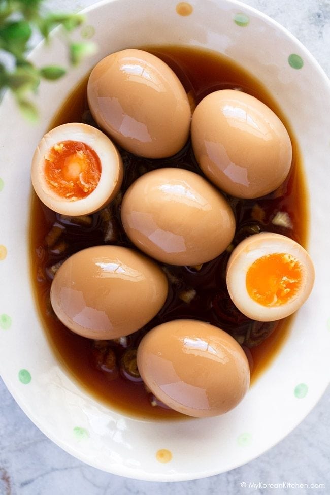 A close-up photo of marinated eggs on an oval plate with sauce.