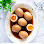Marinated eggs served on an oval plate with savory sauce.