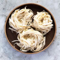 Three bundles of knife-cut noodles placed on a round wooden plate