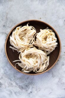 Three bundles of knife-cut noodles placed on a round wooden plate