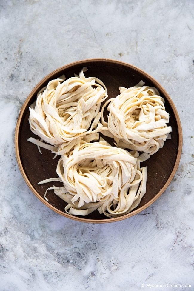 Three bundles of knife-cut noodles placed on a round wooden plate