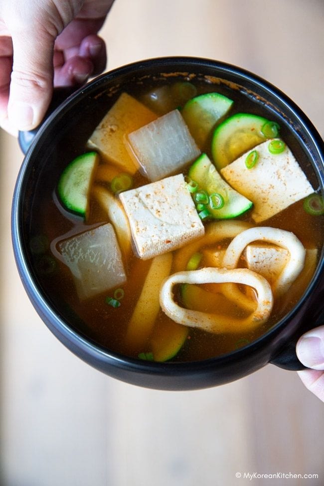 A person holding a black pot filled with Korean squid soup (Ojingeo Guk).